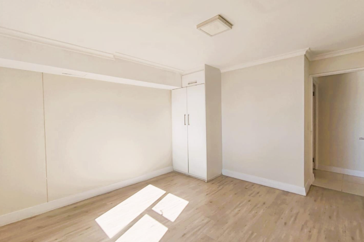 A bright, empty bedroom featuring light-toned laminate flooring, neutral walls, and a built-in wardrobe with clean finishes.