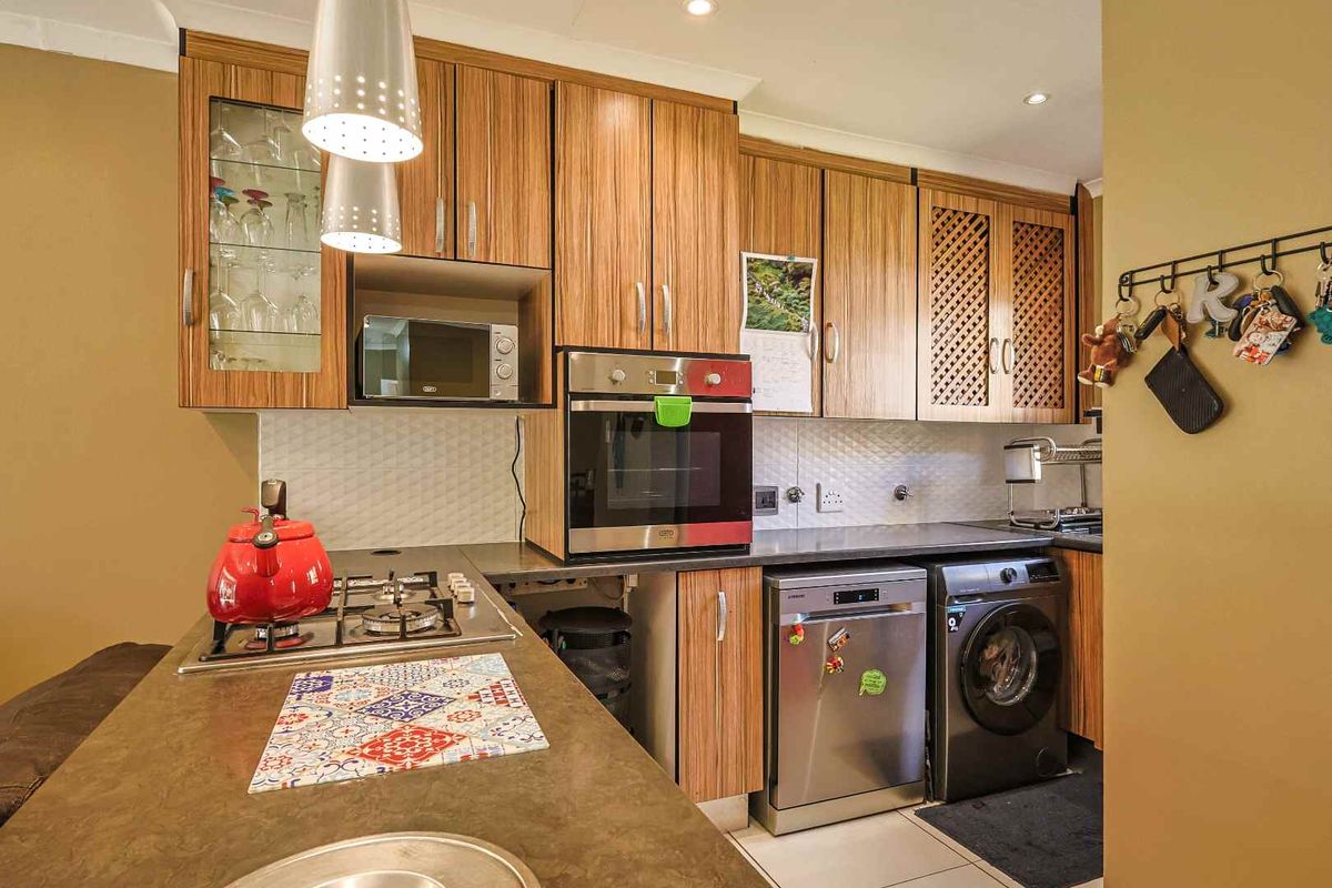 A functional kitchen featuring wood-grain cabinetry, a gas hob, built-in oven, and integrated appliances with a tiled backsplash.