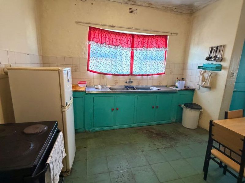 A dated kitchen featuring original cabinetry, a double bowl sink, and tiled flooring, requiring significant renovation and cosmetic updates to improve functionality and aesthetics.