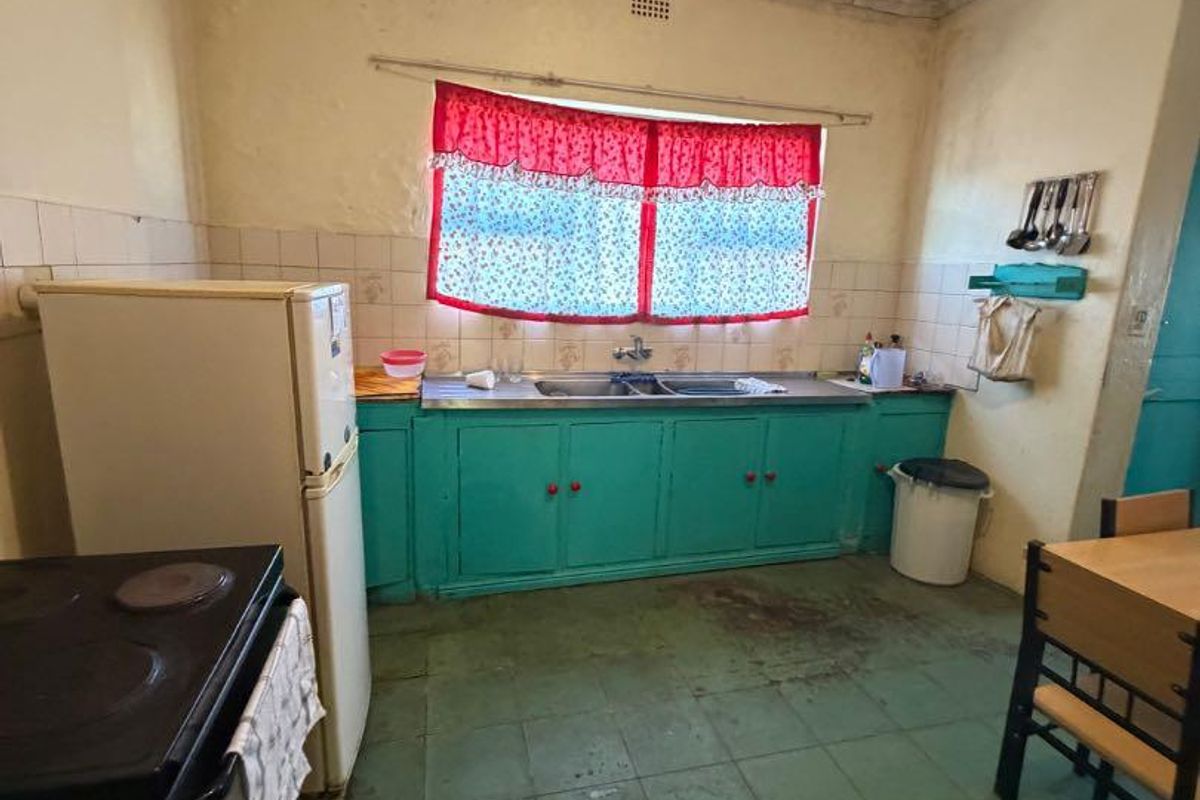 A dated kitchen featuring original cabinetry, a double bowl sink, and tiled flooring, requiring significant renovation and cosmetic updates to improve functionality and aesthetics.