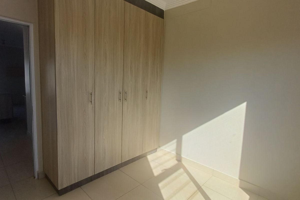 A bright, empty bedroom featuring light wood-finish built-in cupboards and neutral tiled flooring, offering a clean and versatile space.