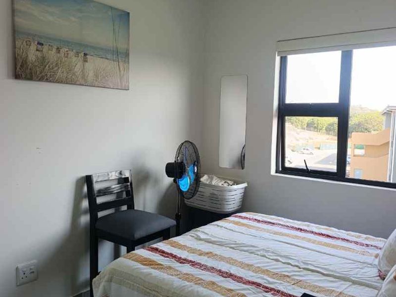A functional bedroom featuring tiled flooring and a large aluminium-framed window with a roller blind, offering natural light and a view of the surroundings.