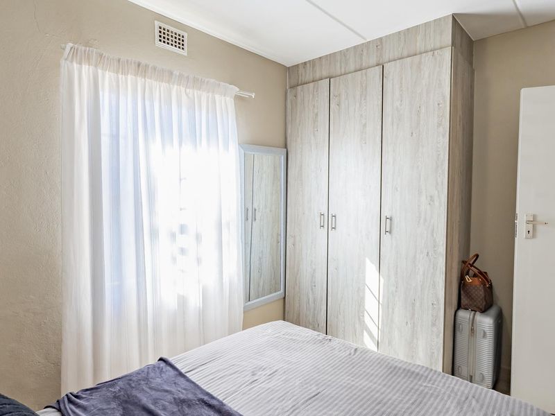 A well-lit bedroom featuring neutral walls and a modern, light-wood finish built-in wardrobe providing ample storage space.