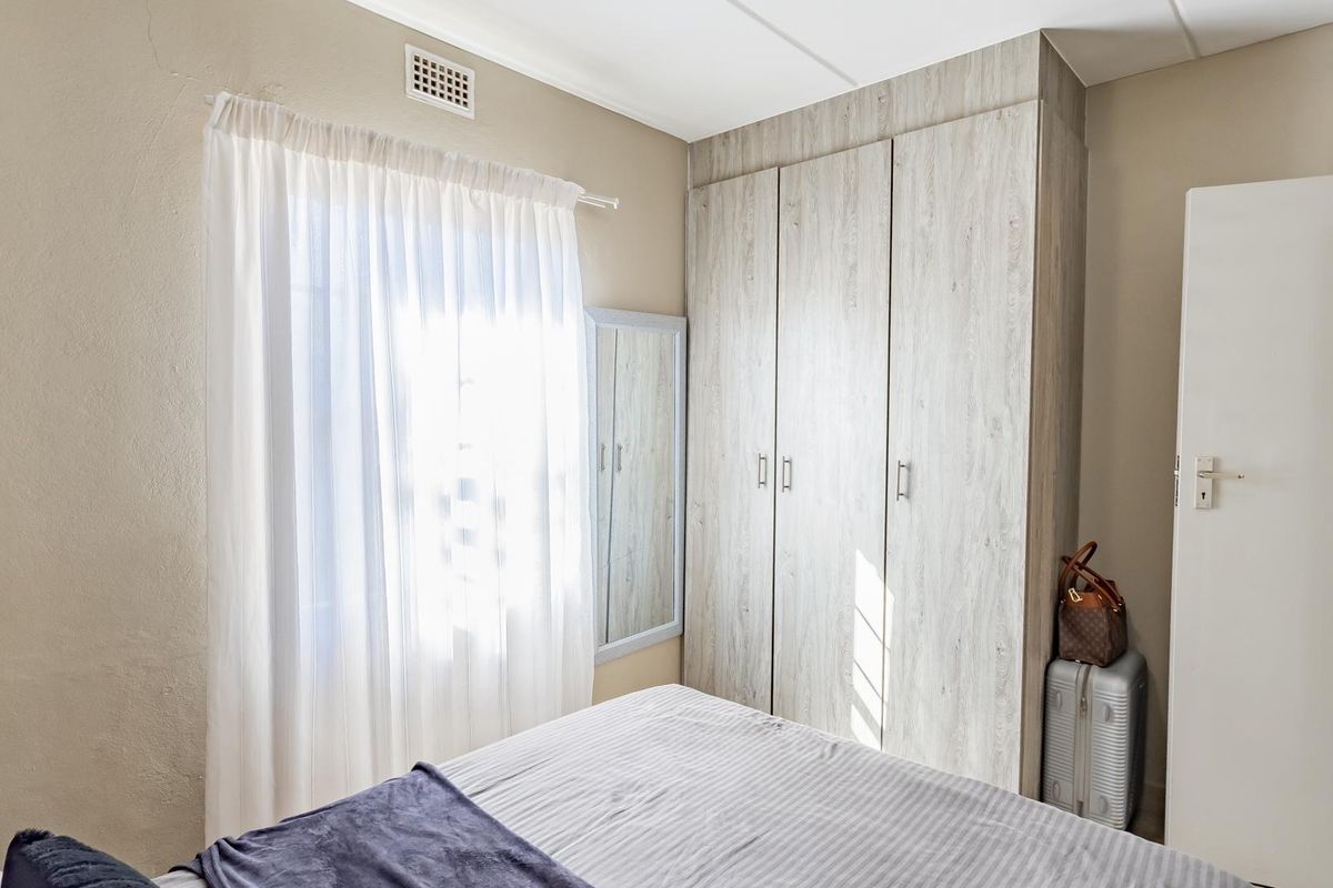 A well-lit bedroom featuring neutral walls and a modern, light-wood finish built-in wardrobe providing ample storage space.
