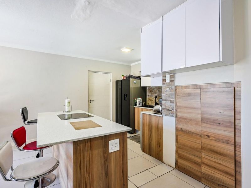 Compact kitchen featuring a central island with an integrated cooktop, wood-finish cabinetry, stone countertops, and tiled flooring.