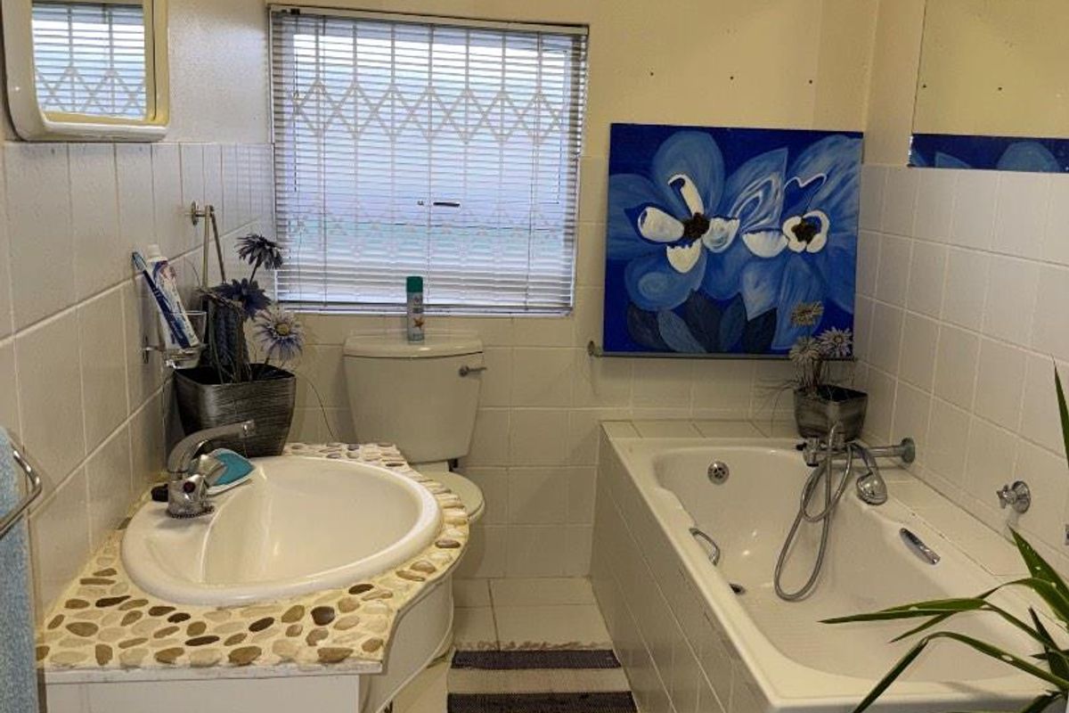 A functional bathroom featuring a built-in bathtub with shower mixer, a vanity basin with stone-look countertop, and a toilet.