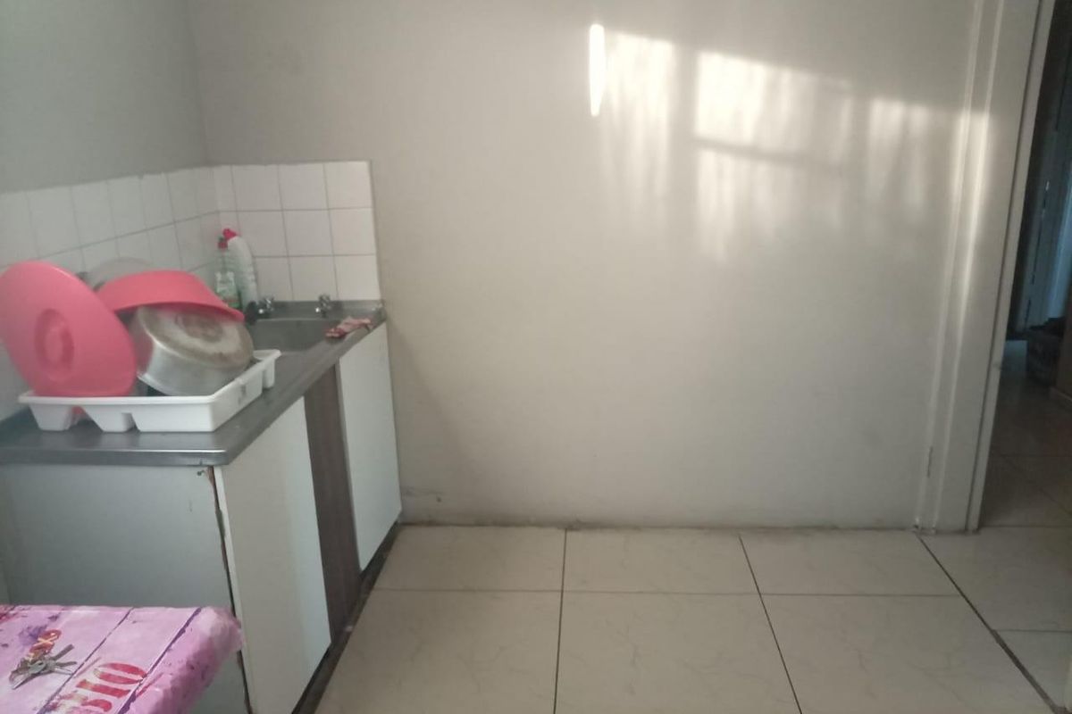 A compact kitchen area featuring basic base cabinetry, a sink with tiled splashback, and neutral floor tiles, offering potential for modernization.