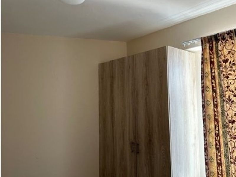 A bedroom featuring a wood-finish built-in wardrobe, neutral wall paint, and a ceiling light fixture.