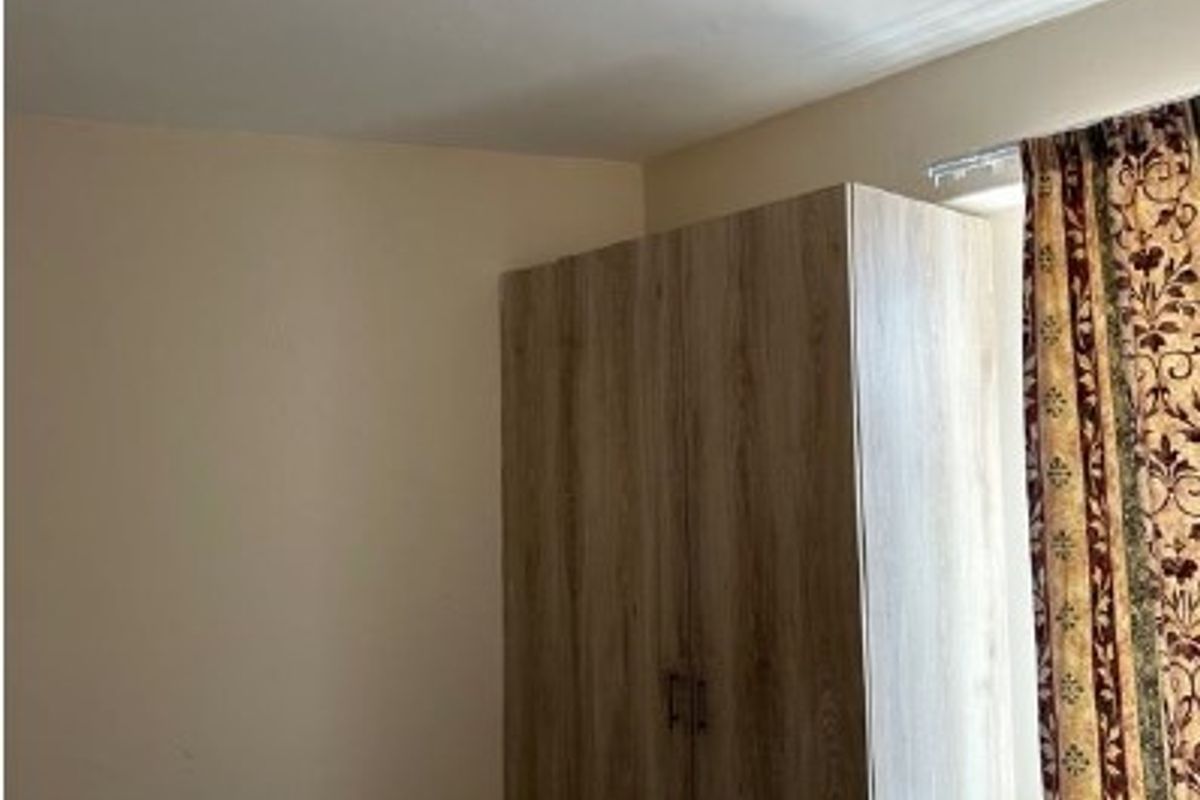 A bedroom featuring a wood-finish built-in wardrobe, neutral wall paint, and a ceiling light fixture.