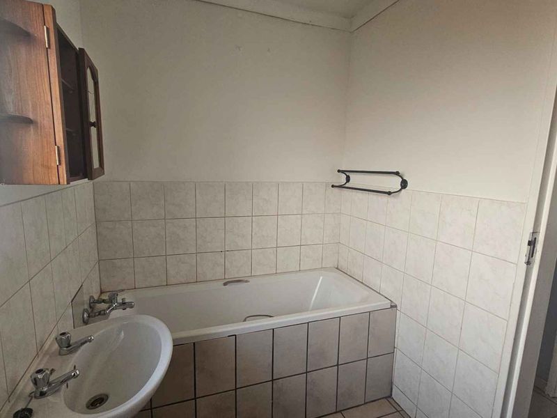 A functional bathroom featuring a bathtub, pedestal basin, and tiled splashbacks. The space is ready for a modern renovation to update the dated finishes.