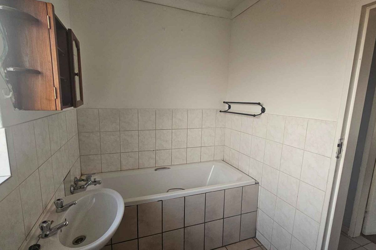 A functional bathroom featuring a bathtub, pedestal basin, and tiled splashbacks. The space is ready for a modern renovation to update the dated finishes.