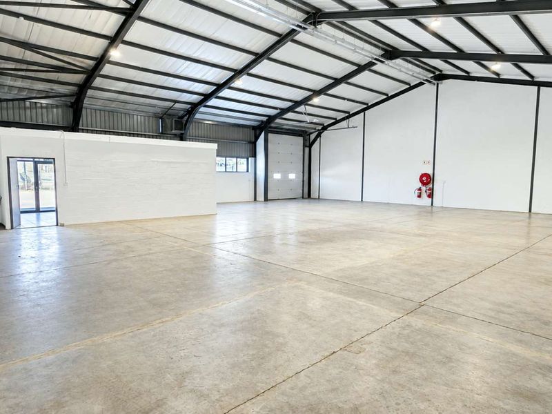 Spacious industrial warehouse featuring high ceilings with exposed steel portal frames, polished concrete flooring, and a large roller shutter door for easy access.