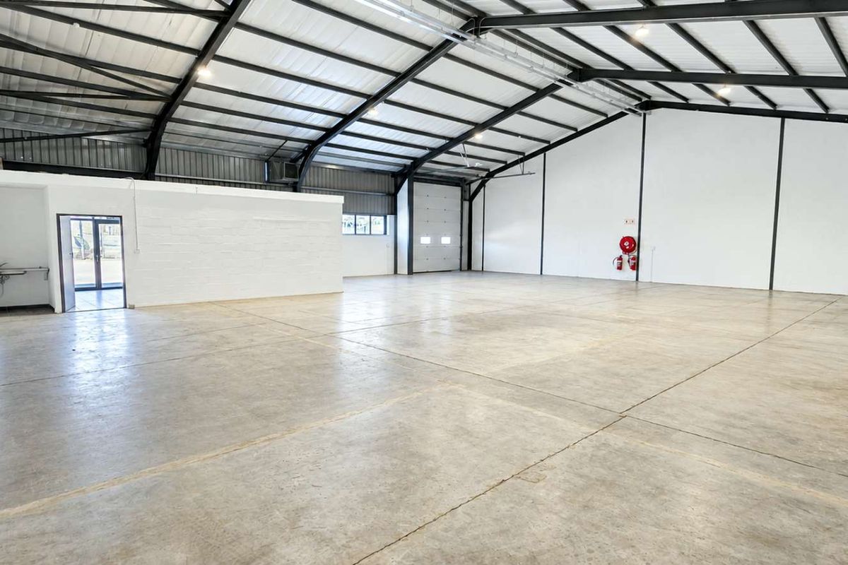 Spacious industrial warehouse featuring high ceilings with exposed steel portal frames, polished concrete flooring, and a large roller shutter door for easy access.
