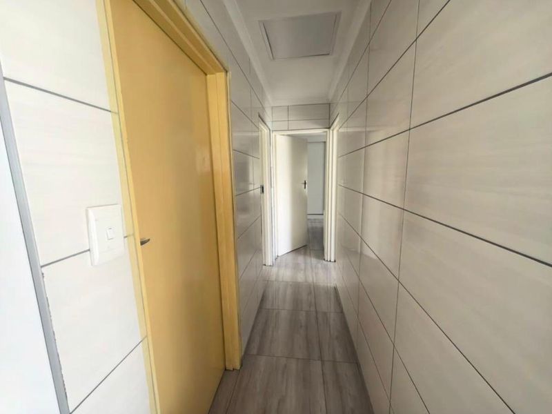 A clean, tiled hallway providing access to multiple rooms, featuring neutral wall tiles and wood-look floor tiles.