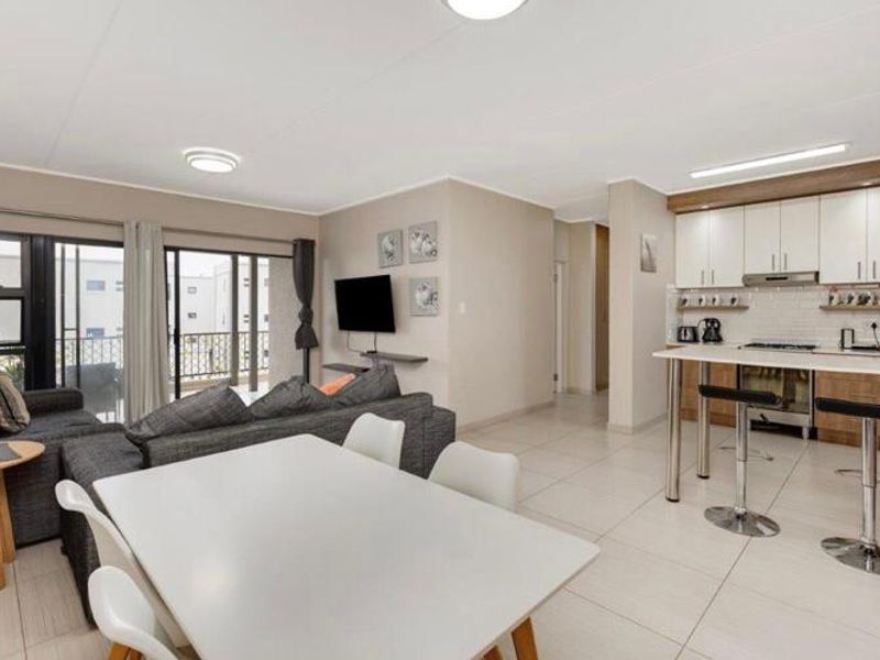 Open-plan living area featuring a modern kitchen with breakfast bar, tiled floors, and sliding doors leading to a balcony.