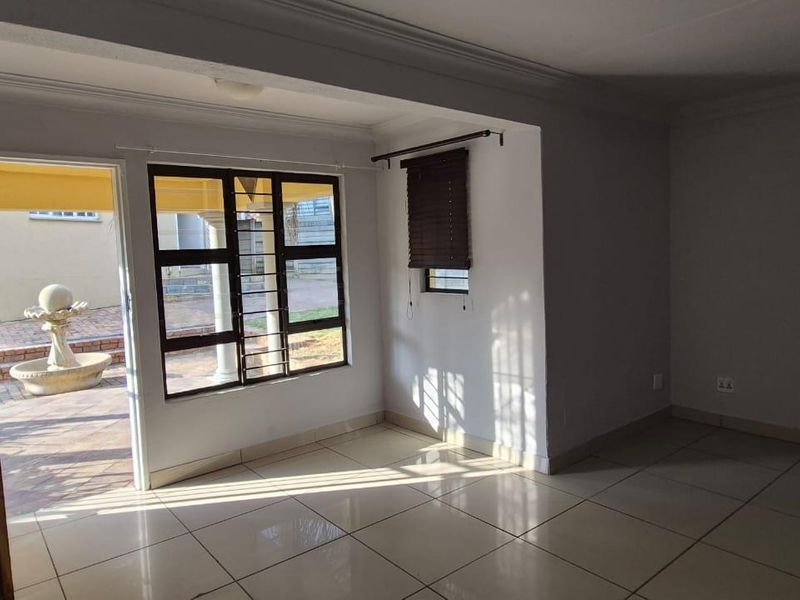 An empty living room featuring tiled flooring, an arched entryway, and large windows with security bars, providing direct access to an outdoor patio area.