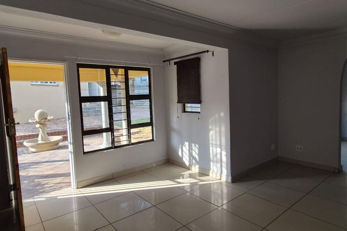 An empty living room featuring tiled flooring, an arched entryway, and large windows with security bars, providing direct access to an outdoor patio area.