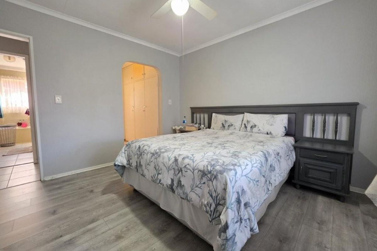 A well-maintained bedroom featuring modern laminate flooring, a ceiling fan, and an arched doorway leading to built-in cupboards.