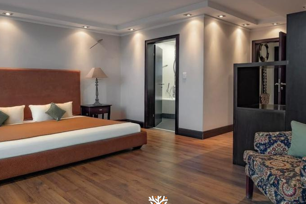 Spacious bedroom featuring warm wood flooring, recessed ceiling lighting, and an en-suite bathroom entrance.