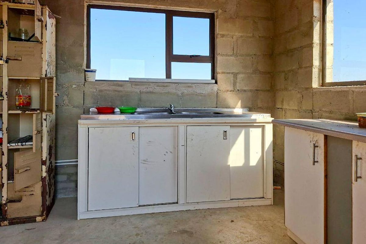 A utility kitchen area featuring exposed concrete block walls, a stainless steel sink, and basic cabinetry in need of renovation.
