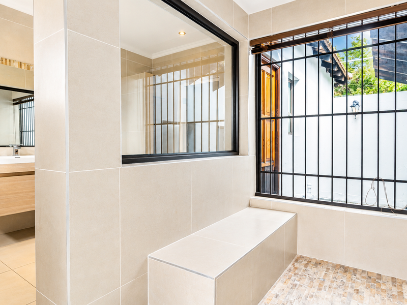 Modern bathroom featuring a built-in vanity, tiled bench seating, and large windows with security bars, finished with neutral ceramic tiles.