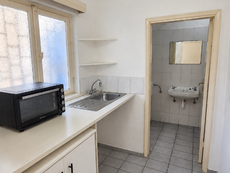 A functional scullery area featuring a stainless steel sink, built-in cabinetry, and tiled flooring, with direct access to an adjacent bathroom.