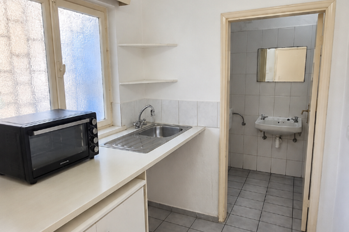 A functional scullery area featuring a stainless steel sink, built-in cabinetry, and tiled flooring, with direct access to an adjacent bathroom.