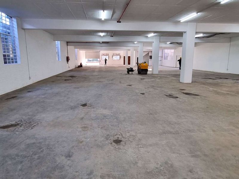 Expansive industrial utility space featuring exposed concrete flooring, structural columns, and high-visibility industrial lighting, suitable for warehouse or workshop operations.