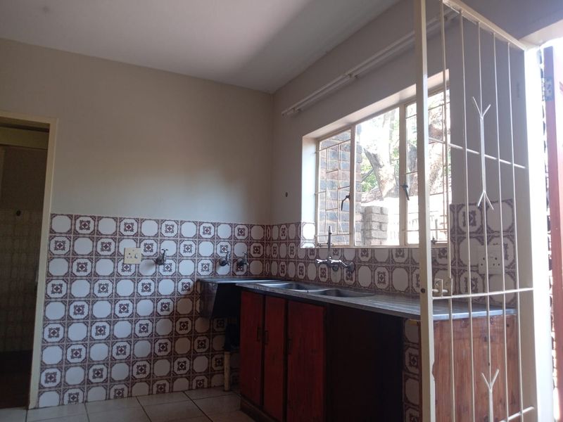 A functional kitchen area featuring built-in wooden cabinetry, a stainless steel sink, and decorative tiled splashbacks, ready for modernization.