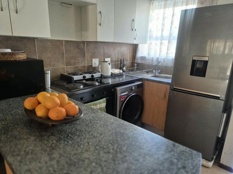 Compact kitchen featuring built-in cabinetry, granite countertops, an electric hob, oven, and a stainless steel sink with a tiled backsplash.
