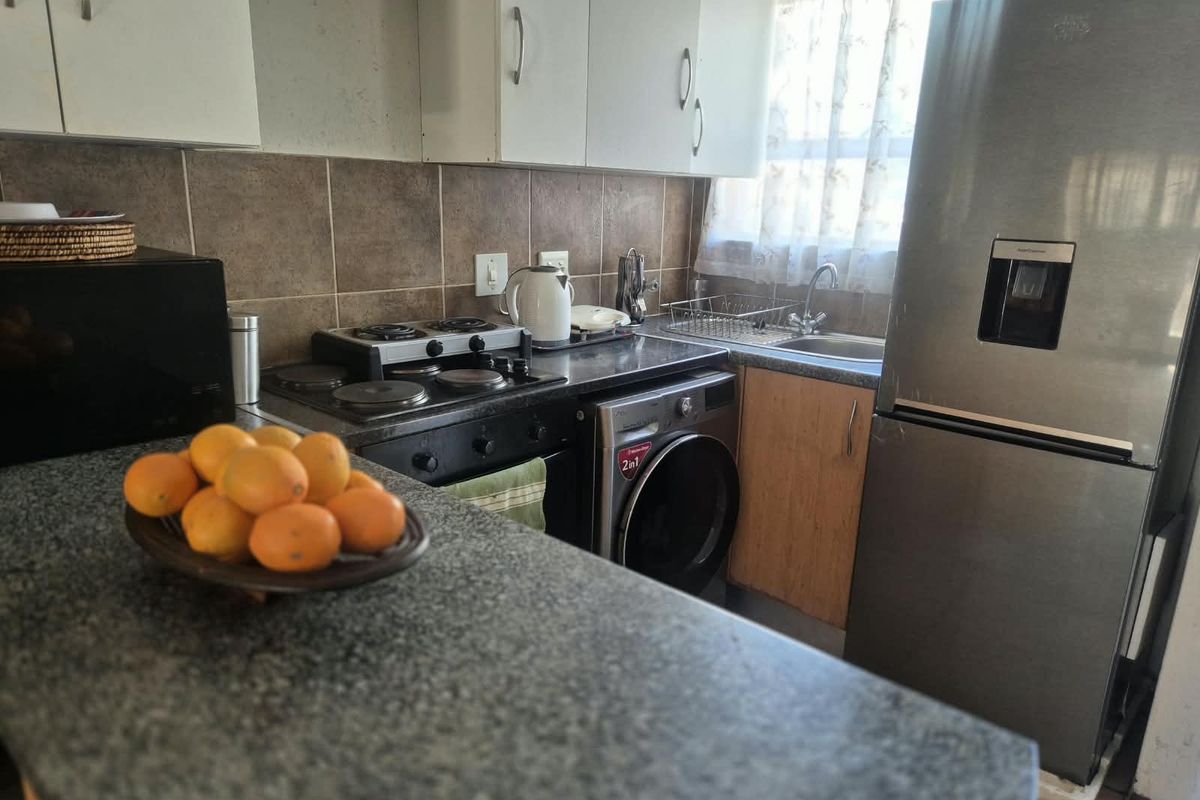 Compact kitchen featuring built-in cabinetry, granite countertops, an electric hob, oven, and a stainless steel sink with a tiled backsplash.