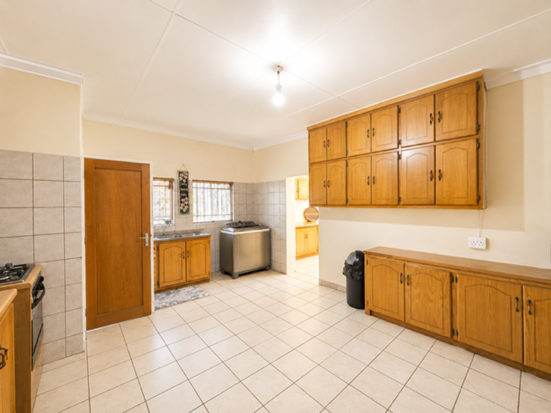 Spacious kitchen featuring extensive wooden cabinetry, tiled flooring, built-in oven and hob, and a functional layout with ample storage space.