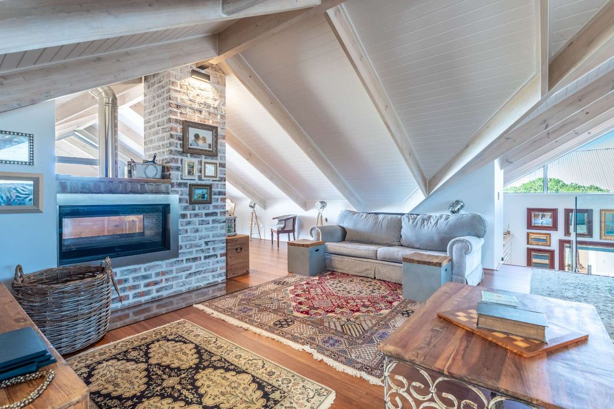 Spacious attic living room featuring a vaulted timber ceiling, exposed brick fireplace with a built-in insert, and warm wood flooring.