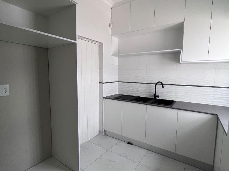 A modern, clean scullery featuring white built-in cabinetry, a black sink with a matching mixer tap, and neutral tiled flooring.