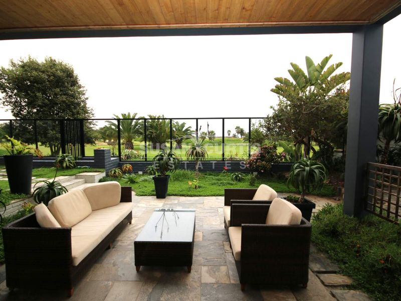A covered outdoor patio featuring stone paving and a timber ceiling, overlooking a landscaped garden and golf course view.