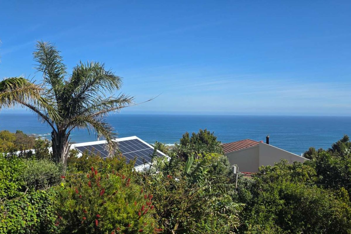 A scenic elevated view overlooking the ocean, featuring lush greenery and visible solar panels on the roof of the property.