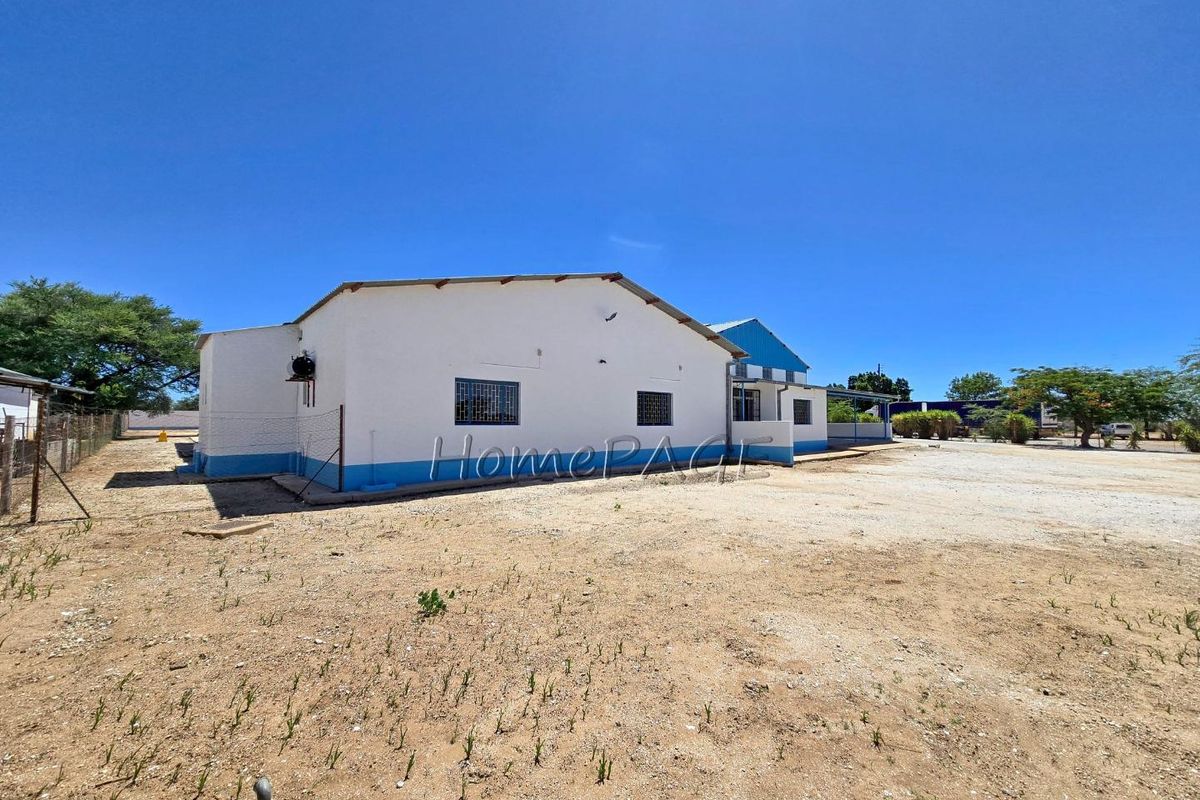 Exterior view of an industrial property featuring a white painted structure with blue trim, metal window grilles, and a large unpaved yard area.