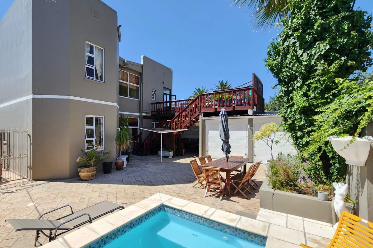 Rear courtyard featuring a swimming pool, paved patio area, and an elevated wooden deck with staircase access to the upper level.