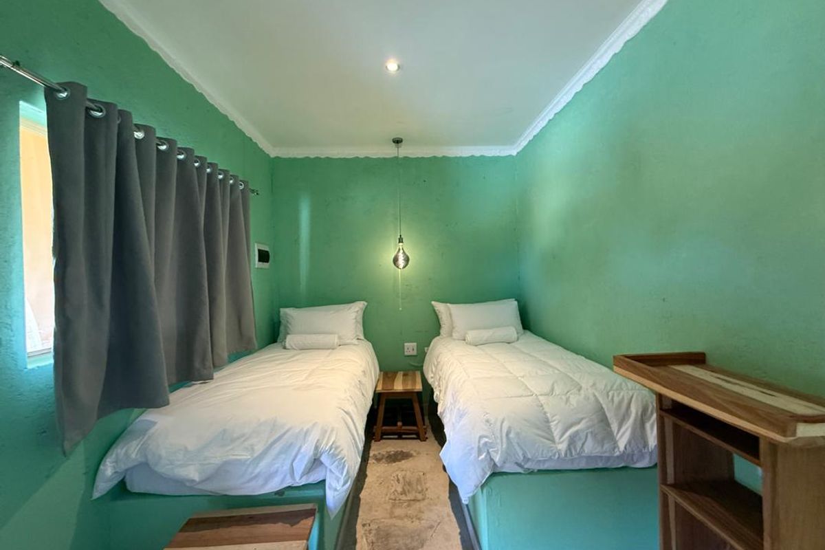 A compact bedroom featuring twin beds, a central pendant light, and green-painted walls with crown molding.
