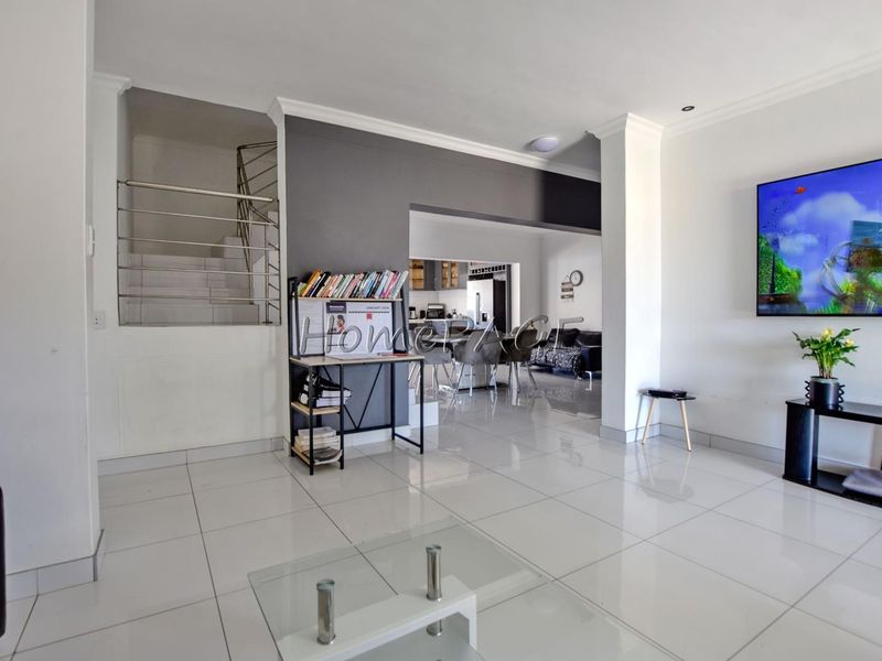Open-plan living area featuring polished tile flooring, a modern staircase with metal balustrade, and a seamless transition into the adjacent kitchen space.