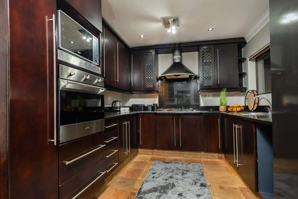 A functional kitchen featuring dark wood cabinetry, granite countertops, a built-in oven, microwave, and a stainless steel extractor fan.