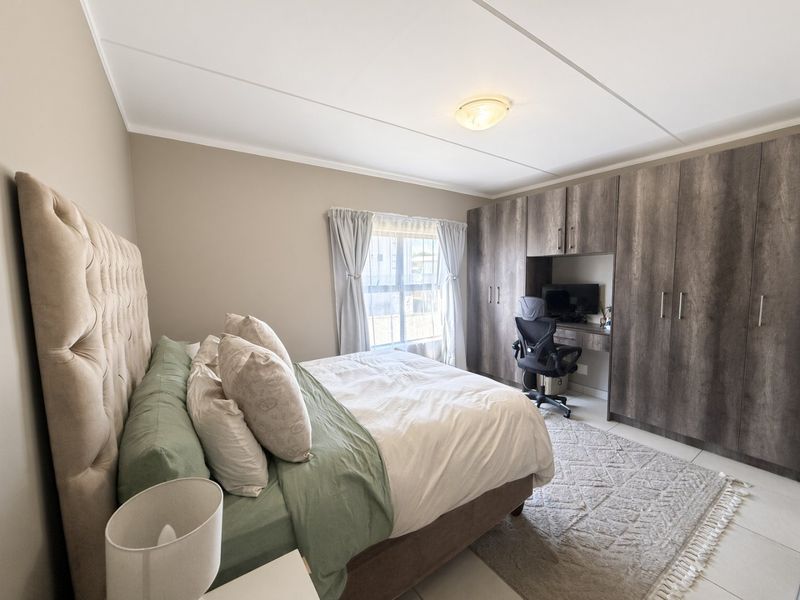 A well-maintained bedroom featuring extensive built-in cabinetry with an integrated desk area, neutral wall finishes, and tiled flooring.