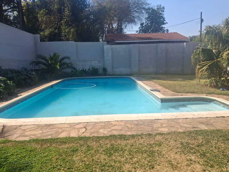 A private swimming pool area featuring stone paving, a surrounding lawn, and high boundary walls for privacy.
