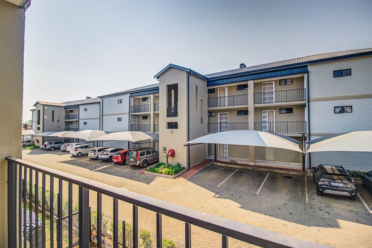 Exterior view of a multi-story apartment complex featuring covered parking bays, paved driveway, and private balconies with metal railings.