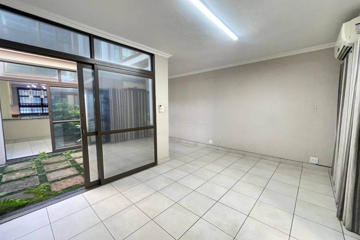 An empty, tiled living area featuring large sliding glass doors that open onto an internal courtyard, equipped with a wall-mounted air conditioning unit.