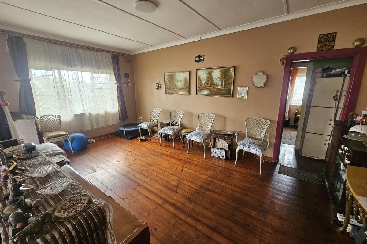 A living room featuring original hardwood flooring, coved ceilings, and a large window with security bars, offering a dated but functional living space.