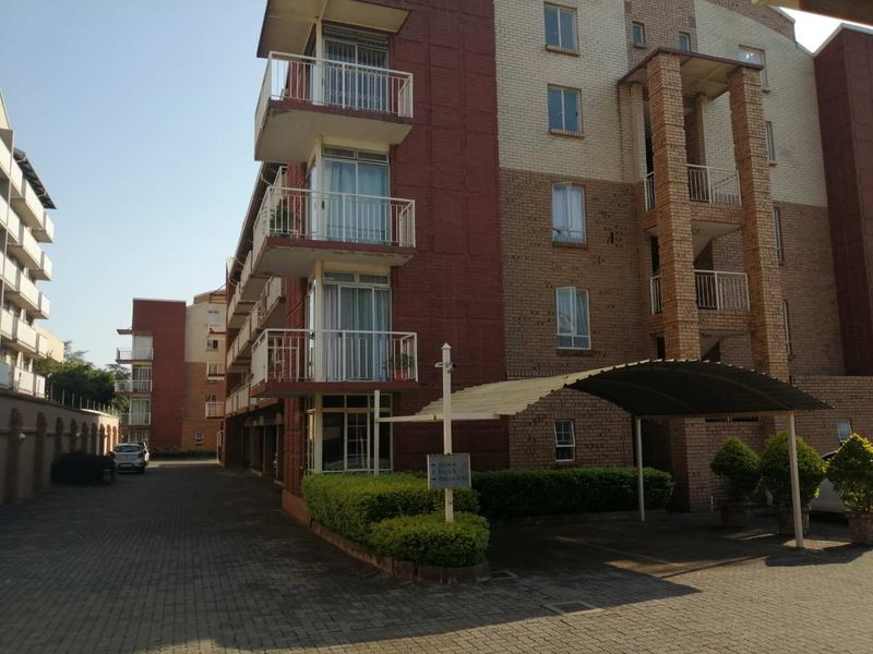Exterior view of a multi-story apartment complex featuring brick facade, private balconies, and a covered carport area with paved driveway access.