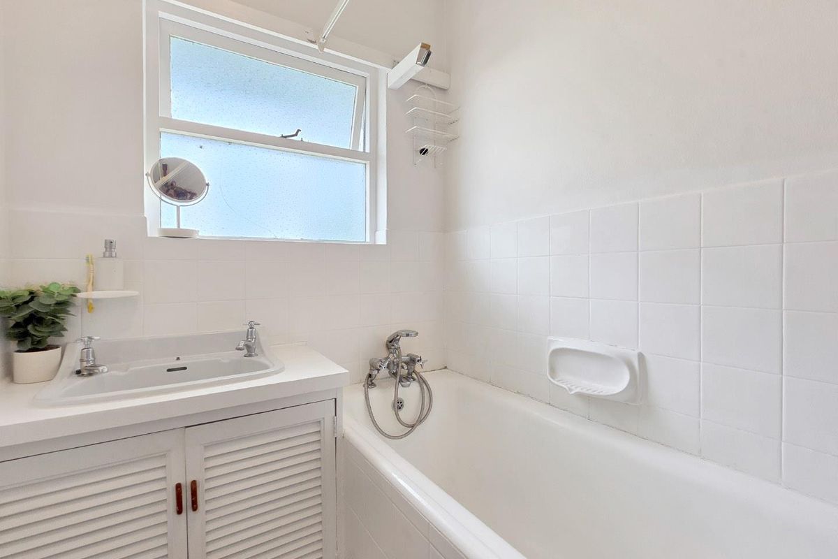A functional bathroom featuring a white bathtub with shower attachment, a vanity cabinet with basin, and classic white wall tiling.