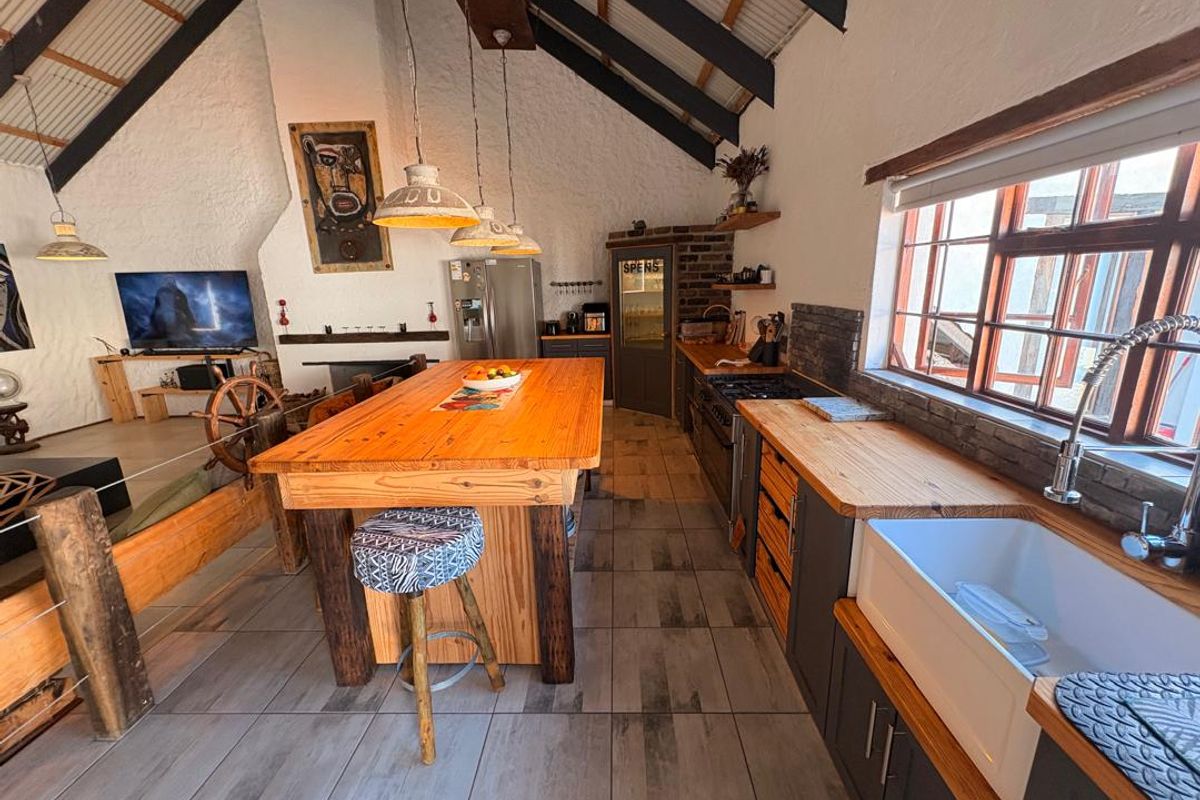 Spacious open-plan kitchen and living area featuring vaulted ceilings with exposed beams, farmhouse sink, timber countertops, and a rustic brick feature wall.