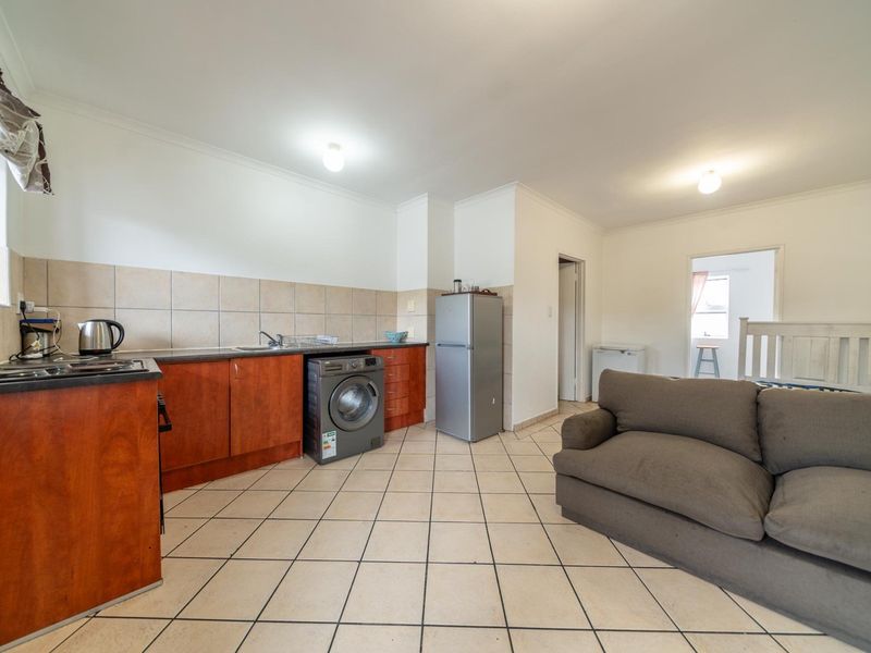 Open plan kitchen and living area featuring tiled flooring, wooden cabinetry, and a tiled backsplash, offering a functional layout for daily living.